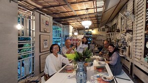 A cozy café with a rustic interior, featuring a long communal table, a decorative vase, and a menu board on the wall. - Village Homestay (Kumphawapi)