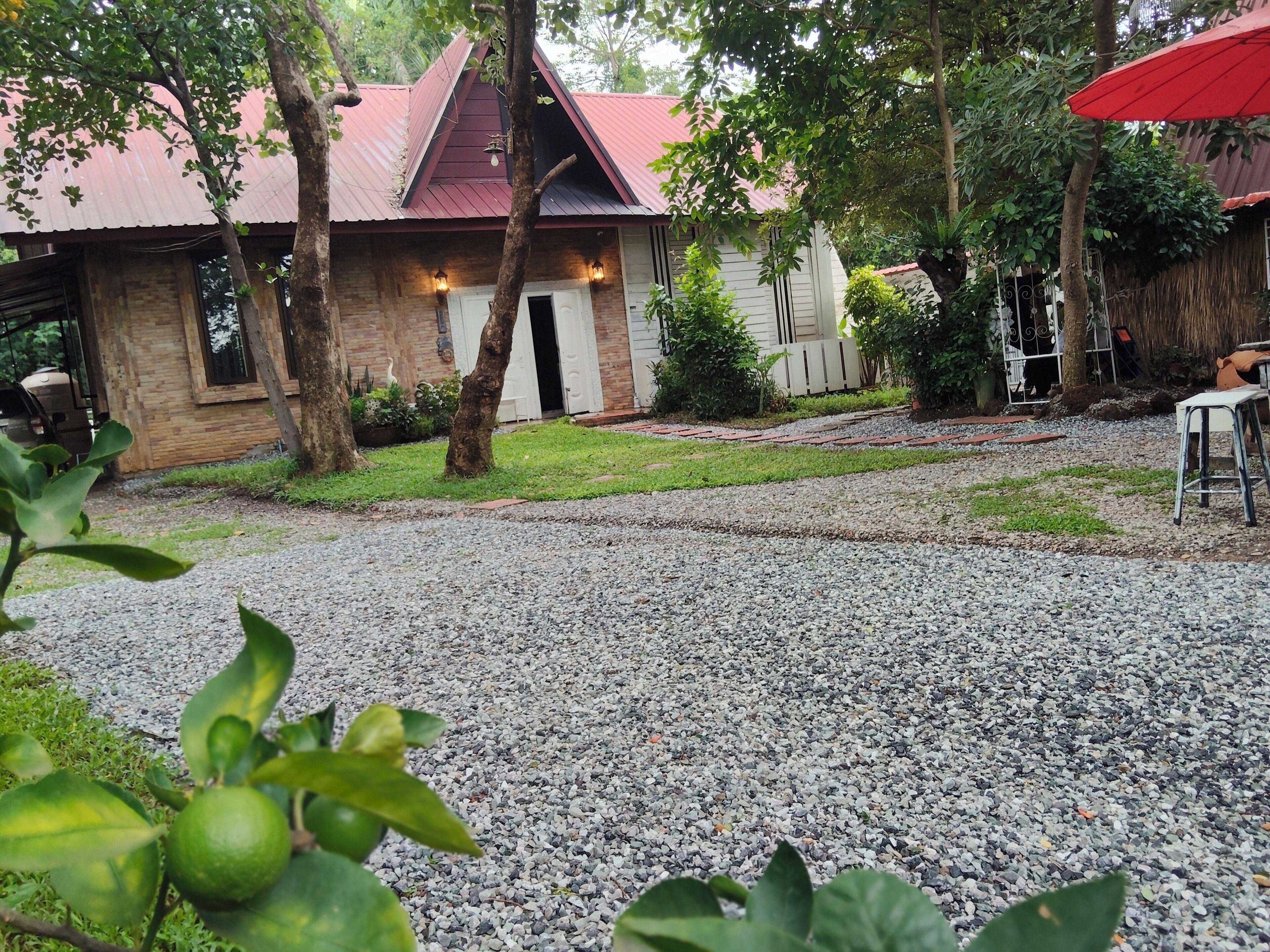 A building with a red roof, a gravel driveway, and a small garden area with trees and plants.