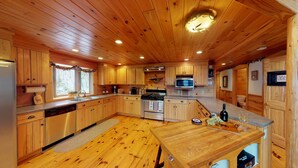 A wooden cabin kitchen with a central island, wooden cabinets, a stainless steel stove, and a microwave.