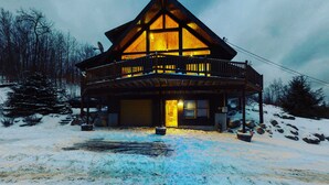 A wooden cabin with a balcony and a garage, surrounded by snow.