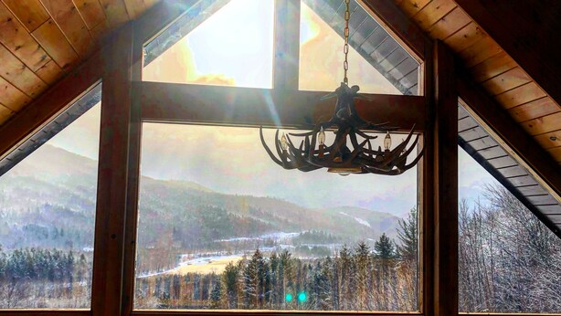 A cabin with a large triangular window offering a view of a snowy landscape and mountains.