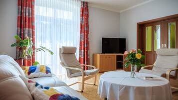 Ein Wohnzimmer mit einer Couch, zwei Sesseln, einem Couchtisch, einem Fernseher und einem Schrank.
