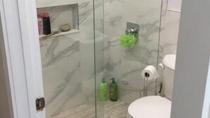 A bathroom with a glass shower enclosure, a toilet, and a small shelf with toiletries. - One bedroom apartment fully modern remodeled/fully furnished  (Hialeah)