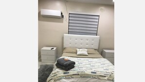 A neatly made bed with a patterned bedspread, a fluffy gray rug, and a white bedside table with a remote control. - One bedroom apartment fully modern remodeled/fully furnished  (Hialeah)