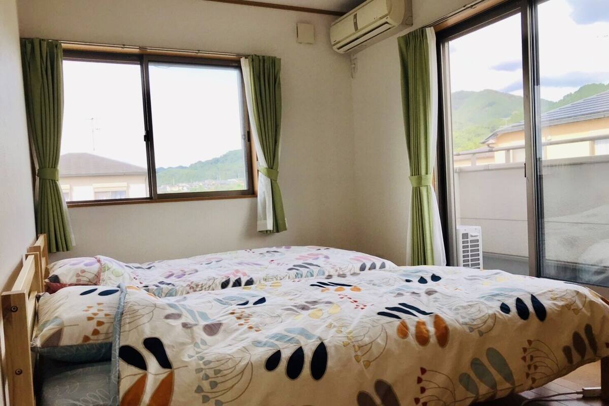 Une chambre avec deux lits, une fenêtre avec des rideaux, un appareil de climatisation et une vue sur des collines.