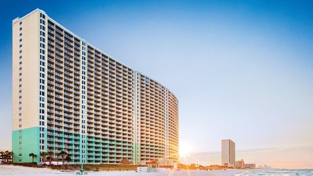 Korkea hotellirakennus, jossa on useita parvekkeita, näkymä rannalle ja auringonlasku taustalla.