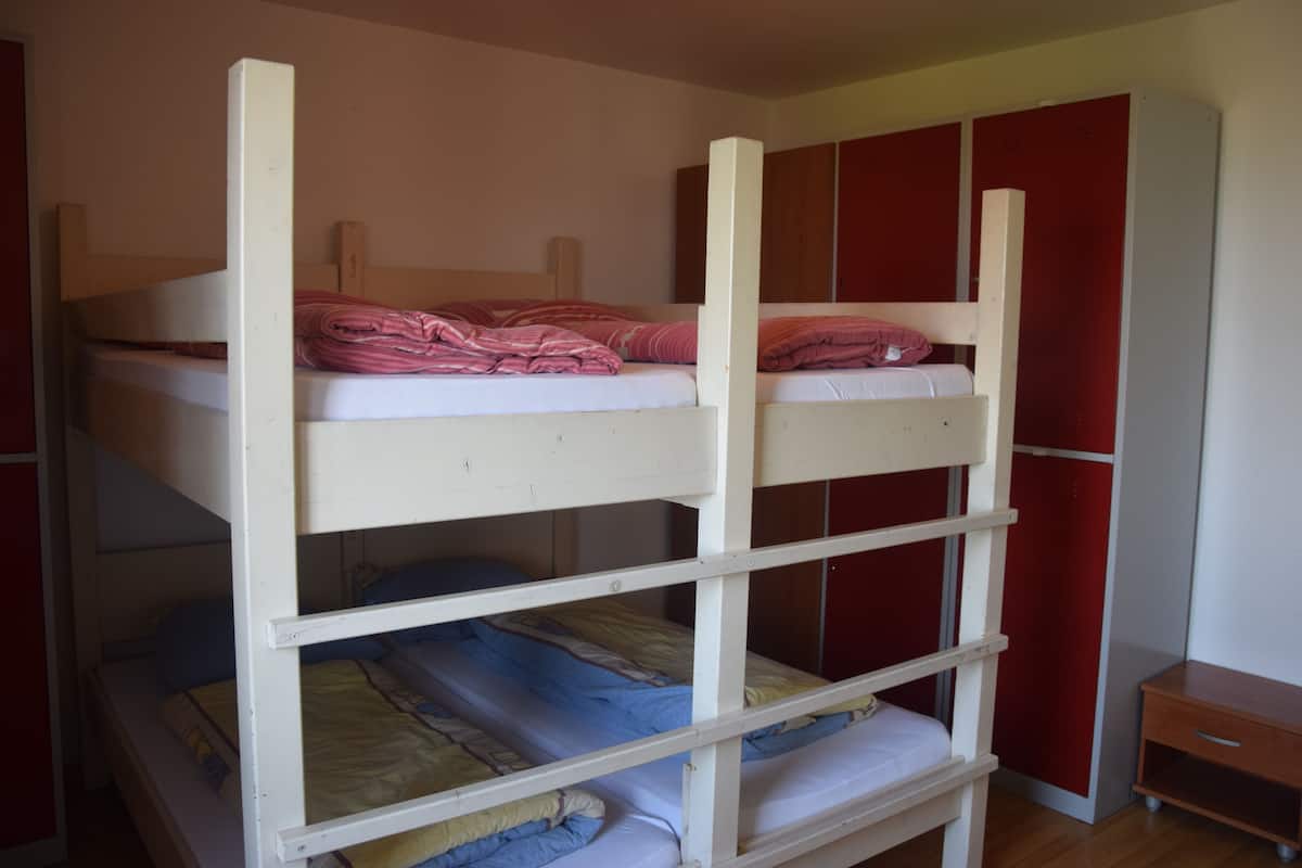 A bunk bed with three levels, wooden headboards, and a small wooden table beside it.