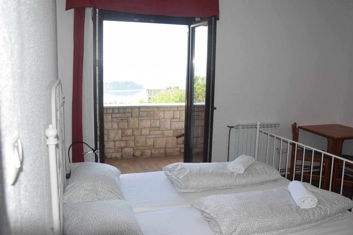 A room with two beds, a small table, and a view of the outdoors.