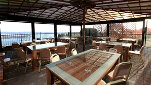 En udendørs terrasse med borde og stole, et overdækket område og havudsigt.