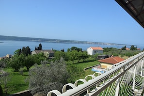 A balcony with a view of a coastal landscape, including trees, a swimming pool, and buildings in the distance.