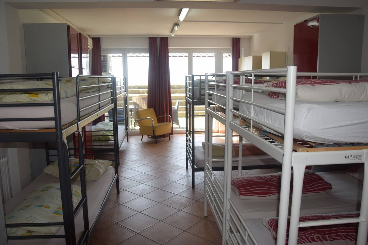 A dormitory room with bunk beds, a chair, and a view of the outdoors through a window.
