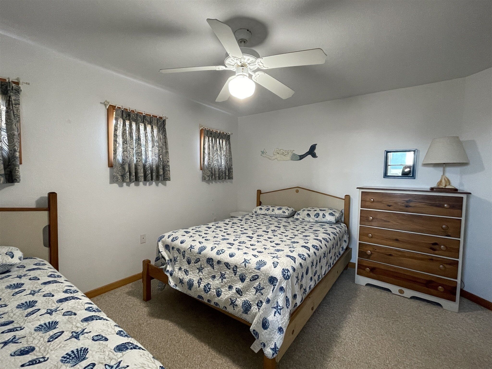 A bedroom with a bed, a dresser, a ceiling fan, and curtains.