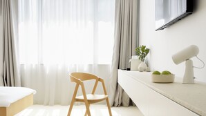 Een strak ingerichte hotelkamer met een bed, een bureau met lamp, een stoel en een aan de muur bevestigde televisie.