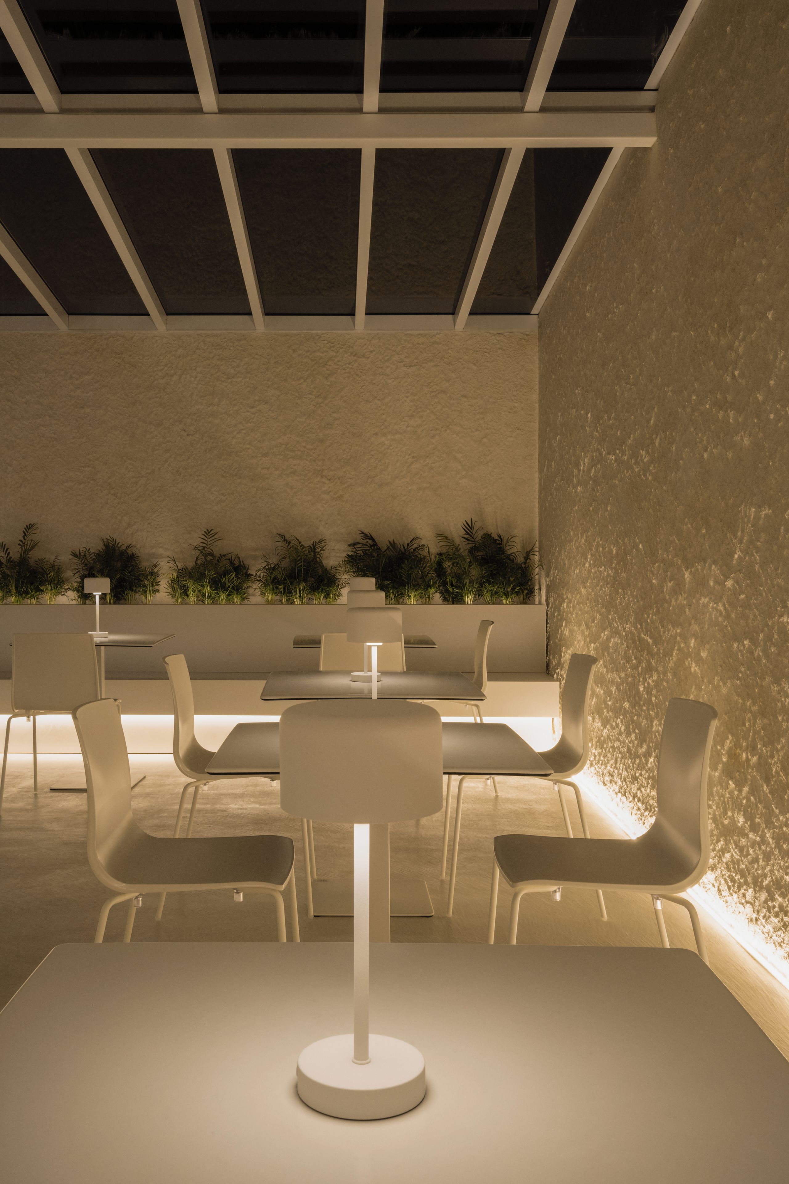 A modern indoor dining area with a central table, white chairs, and a textured wall.