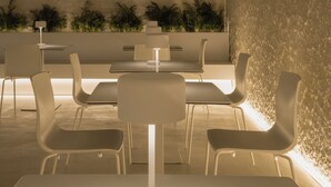 A modern indoor dining area with a central table, white chairs, and a textured wall. - Hotel Hello Plovdiv (Plovdiv)