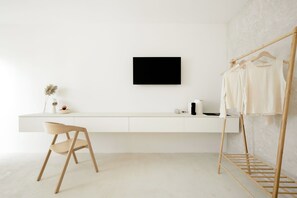 A minimalist room with a white desk, a chair, a wall-mounted TV, and a wooden drying rack with clothes. - Hotel Hello Plovdiv (Plovdiv)