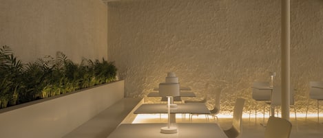 A modern interior with a dining area featuring white tables and chairs, a central white lamp, and a textured wall with a green plant wall.