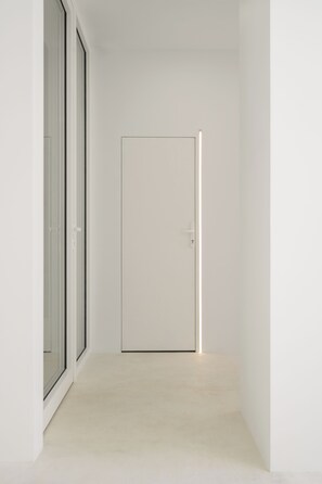 A narrow hallway with a closed door at the end, a sliding glass door on the left, and a light fixture above the door. - Hotel Hello Plovdiv (Plovdiv)