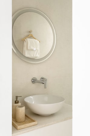 A bathroom with a round mirror, a white sink, a towel hanging on a wooden hanger, and a soap dispenser on a wooden tray. - Hotel Hello Plovdiv (Plovdiv)