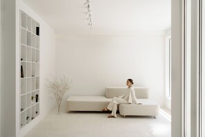 A minimalist living room with a white sofa, a built-in bookshelf, and a vase with dried branches. - Hotel Hello Plovdiv (Plovdiv)
