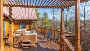Eine Holzterrasse mit Whirlpool, Stühlen und einer Pergola.