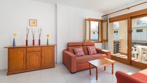 Ein Wohnzimmer mit einer Couch, einem Holzschrank und einem Tisch. Ein Fenster bietet Blick auf Gebäude.