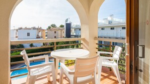 Un balcón con una mesa y sillas blancas, una piscina y vistas de edificios circundantes.