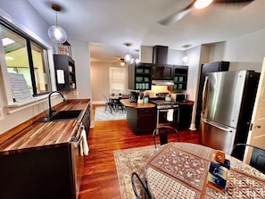 A modern kitchen with a central island, stainless steel appliances, and a dining area with a patterned tablecloth. - Historic Moog Farmhouse – 4-Bedroom Retreat Near Downtown Asheville (Asheville)