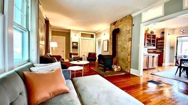 A spacious living room with a large sofa, a coffee table, and a fireplace. There is a kitchen area visible in the background.