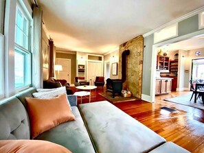 A spacious living room with a large sofa, a coffee table, and a fireplace. There is a kitchen area visible in the background. - Historic Moog Farmhouse – 4-Bedroom Retreat Near Downtown Asheville (Asheville)