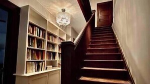 A staircase with wooden steps leading to a landing, flanked by white bookshelves and a chandelier.