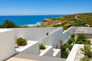 A modern building with white walls and a rooftop garden with plants and rocks.