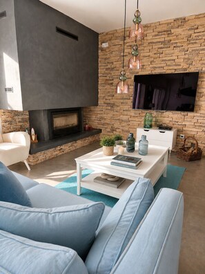 A modern living room with a stone wall, a fireplace, a flat-screen TV, a white coffee table, and blue sofas.