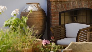 A rustic outdoor seating area with a brick fireplace, wooden furniture, and potted plants.
