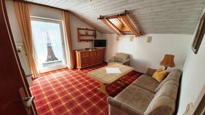 A room with a checkered floor, a sofa, a wooden cabinet, a television, and a window with curtains. - Ferienwohnung Rauschberg Balk., Küche, 1 Schlaf- u. 1 Wohn-/schlafz., max 4 P (Ruhpolding)