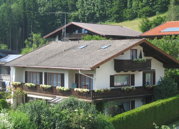 Een chalet met twee verdiepingen, een schuin dak, houten balkonleuningen en bloembakken.