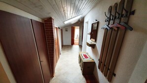 A narrow hallway with wooden doors, a brick wall, a wooden bench, and a coat rack with hangers. - Ferienwohnung Rauschberg Balk., Küche, 1 Schlaf- u. 1 Wohn-/schlafz., max 4 P (Ruhpolding)