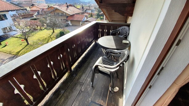 A balcony with a wooden floor, two plastic chairs, and a table. - Ferienwohnung Rauschberg Balk., Küche, 1 Schlaf- u. 1 Wohn-/schlafz., max 4 P (Ruhpolding)