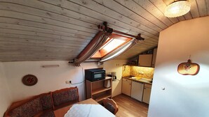 A cozy room with a wooden ceiling, a dining table with a white tablecloth, a patterned sofa, and a kitchen area with a microwave and a sink. - Ferienwohnung Rauschberg Balk., Küche, 1 Schlaf- u. 1 Wohn-/schlafz., max 4 P (Ruhpolding)