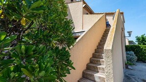 Una escalera que lleva a un edificio de fachada color beige y un árbol con hojas verdes a su lado.