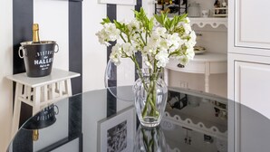 Ein Essbereich mit einem Glastisch, an der Wand befinden sich Schwarz-Weiß-Fotos und ein Blumenstrauß mit weißen Blüten.