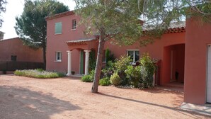 Ein Gebäude mit roter Fassade, einer Säulenveranda und einem Garten mit verschiedenen Pflanzen und einem Baum.