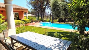 Eine Terrasse mit Tisch und Stühlen, ein Schwimmbecken und ein Haus im Hintergrund.
