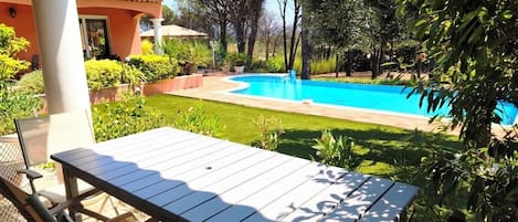 A patio with a table and chairs, a swimming pool, and a house in the background.
