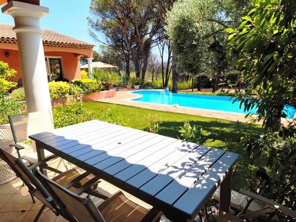 A patio with a table and chairs, a swimming pool, and a house in the background. - Charming Apt. in a villa ideally located in a pine woods near the sea (Var)