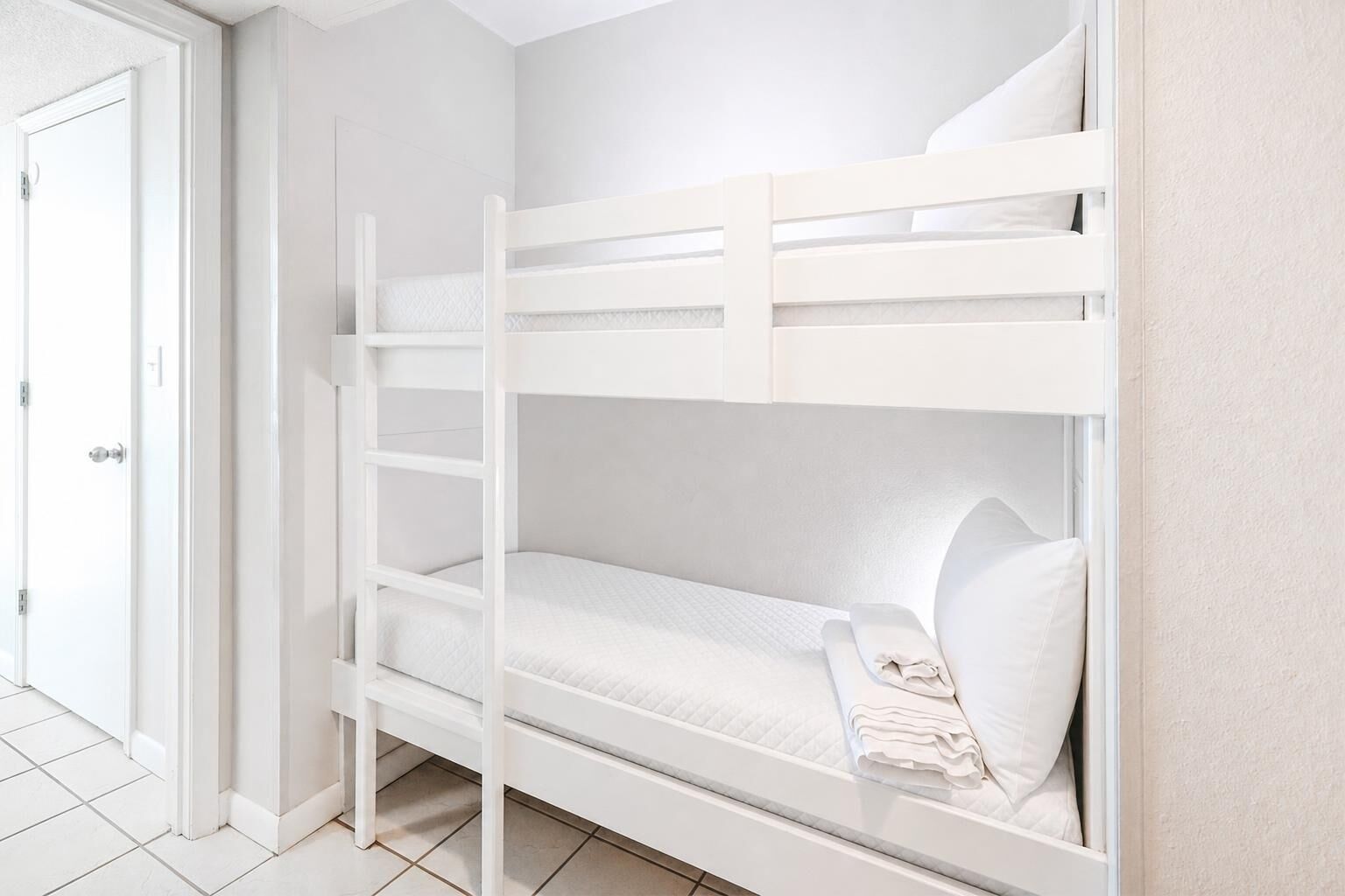 A bunk bed with white bedding and a door to the left.