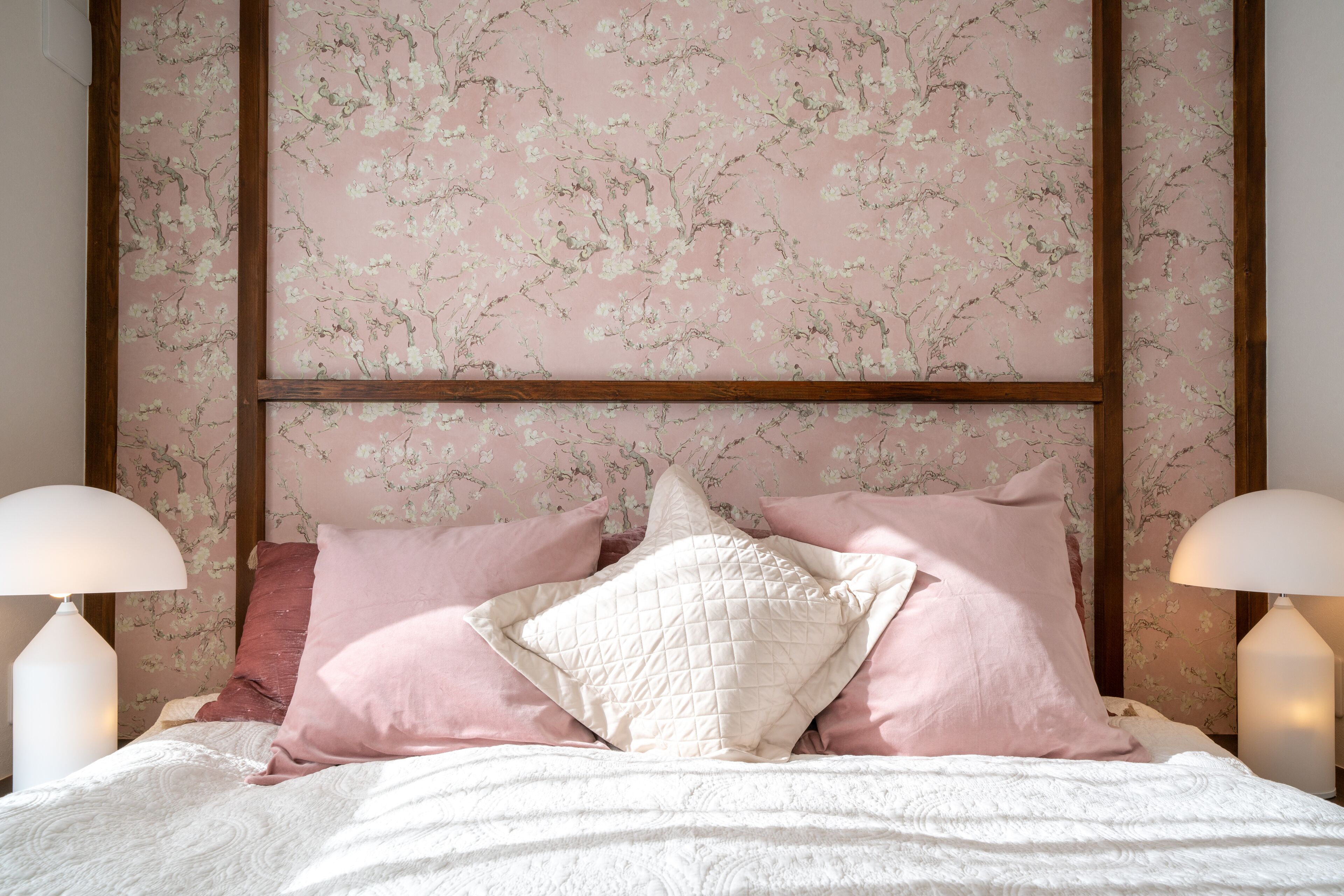 A bedroom with a floral wallpaper, a wooden headboard, and two bedside lamps.