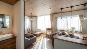 Una sala de estar moderna con techo de madera, un sofá, una mesa de comedor con sillas y una cocina con fregadero y armarios.
