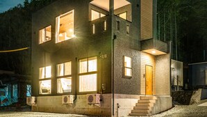 Un edificio moderno de dos pisos con amplias ventanas, una puerta de madera y una escalera que conduce a la entrada.