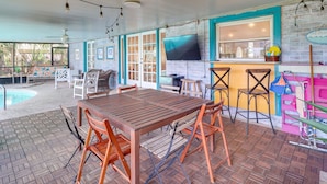 Un patio al aire libre con una mesa y sillas de madera, una piscina y una zona de bar con taburetes.
